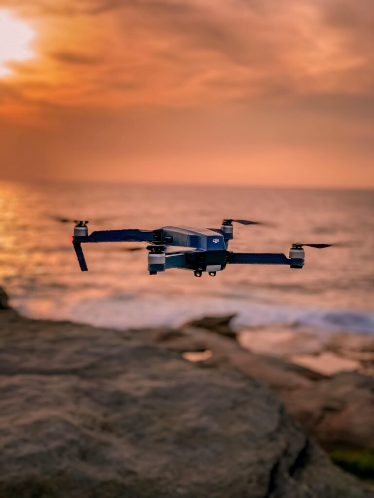 pexels-photo-1809576-1809576 A drone hovers over a rocky shoreline with a stunning sunset backdrop, creating a serene atmosphere.